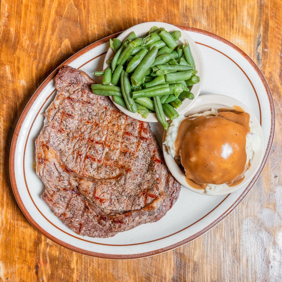 Grilled steak, green beans, and mashed potatoes with gravy on a plate on a wooden table.