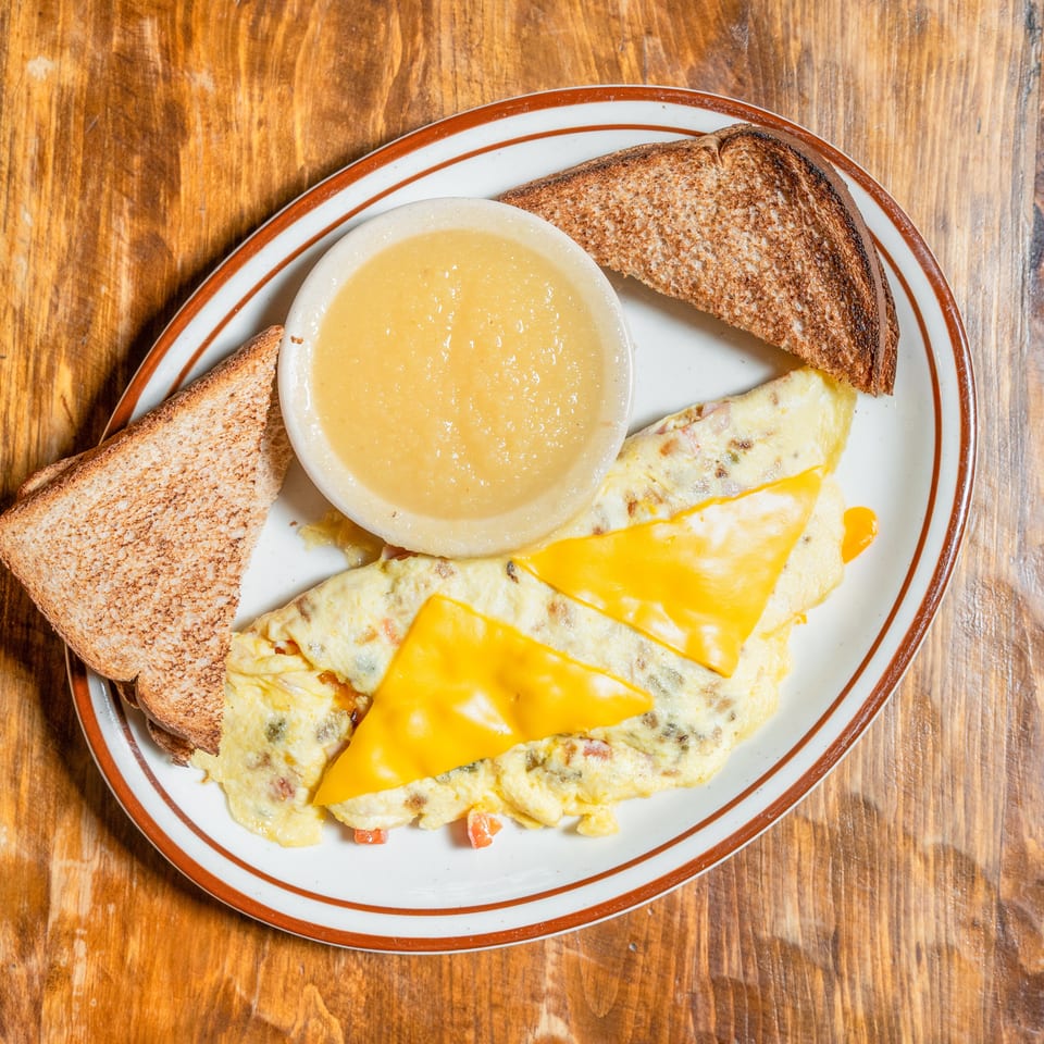 Breakfast plate with a cheese omelet, two toast slices, and a side of applesauce.