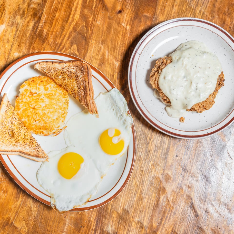 Breakfast plate with fried eggs, hash browns, toast, and a separate plate of chicken fried steak with gravy.