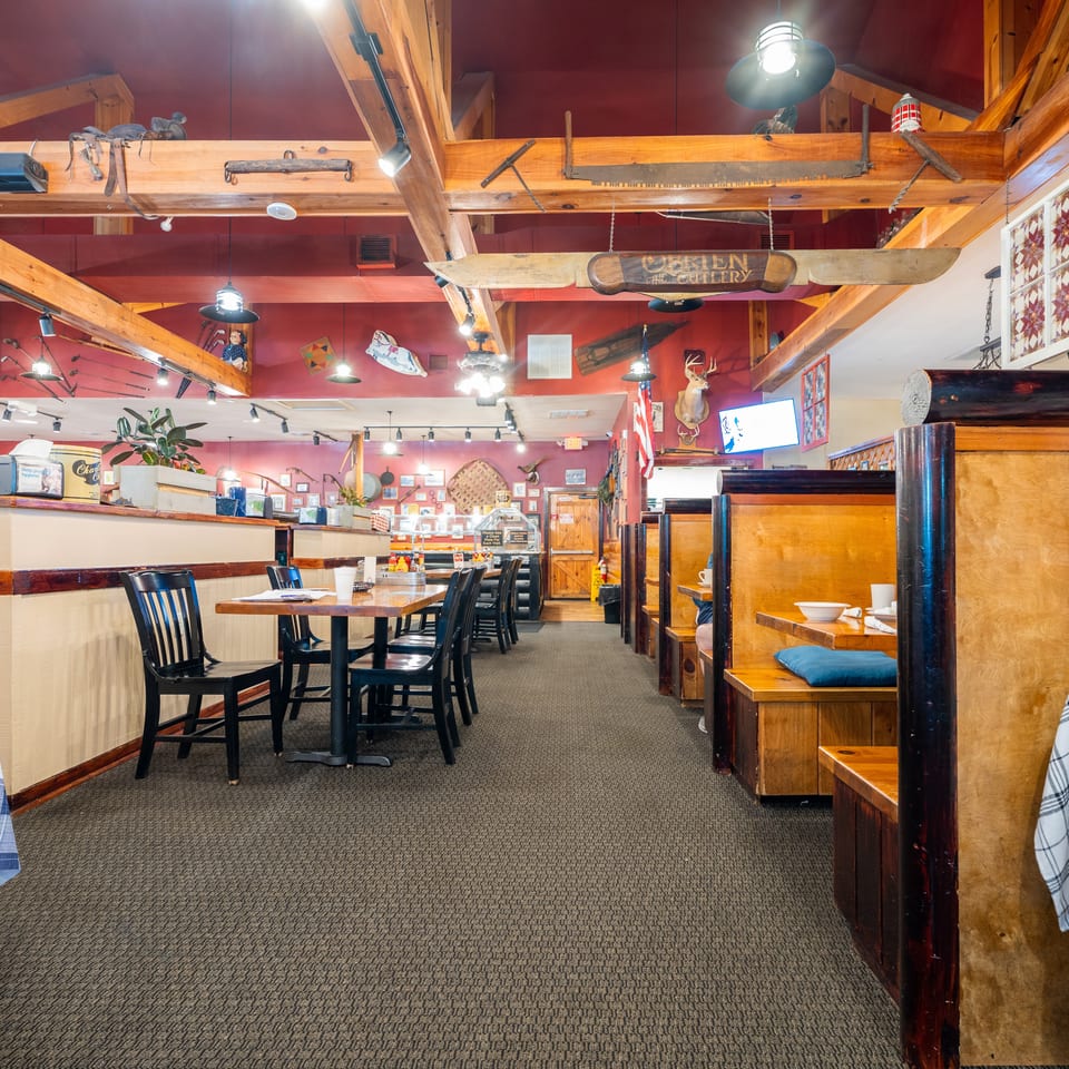 Rustic restaurant interior featuring red walls, wooden beams, tables, chairs, and cozy booth seating.