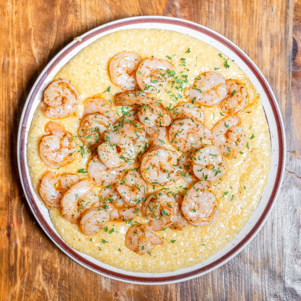 Plate of shrimp and grits garnished with parsley on a wooden table.