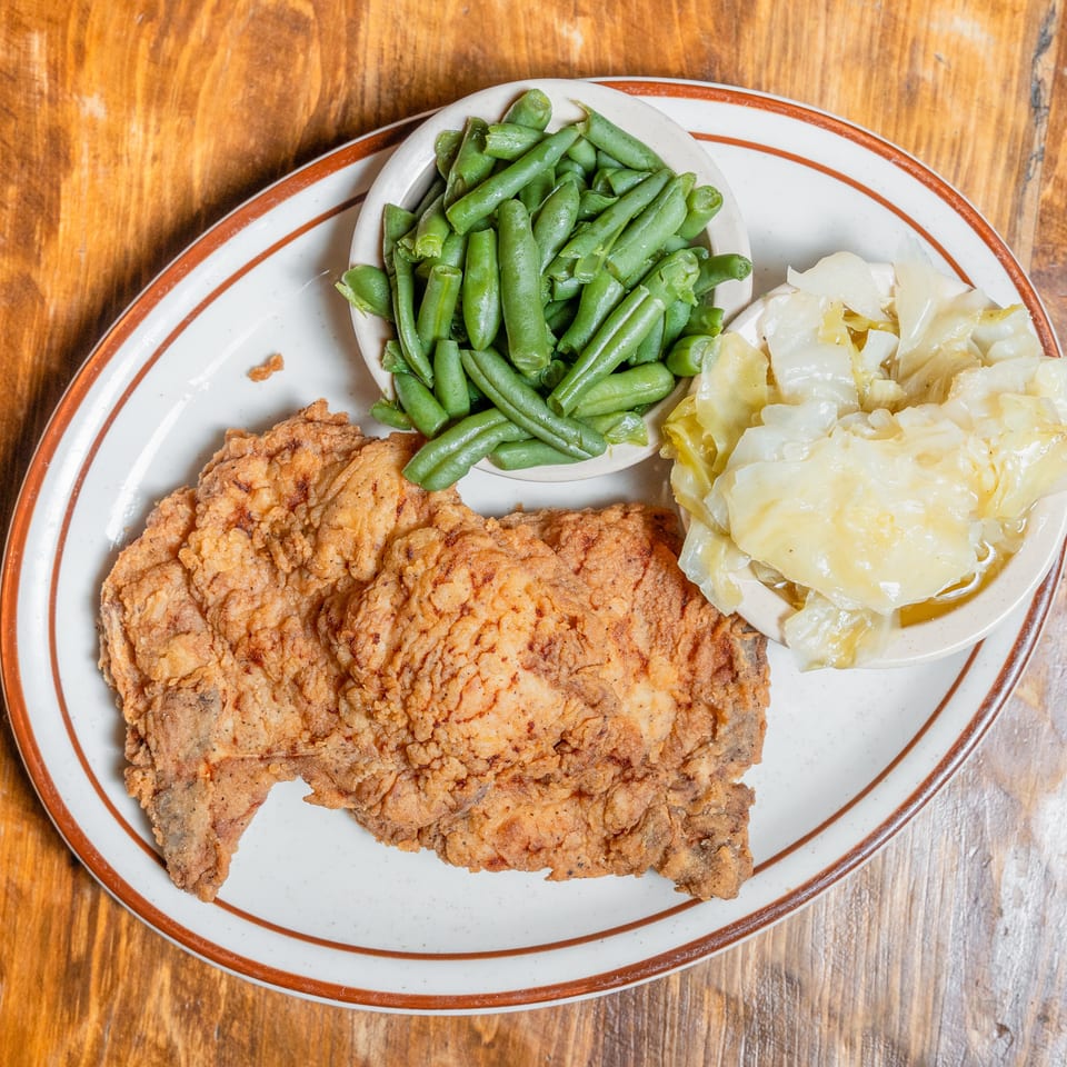 Crispy fried pork chops served with green beans and stewed cabbage on a rustic wooden table.