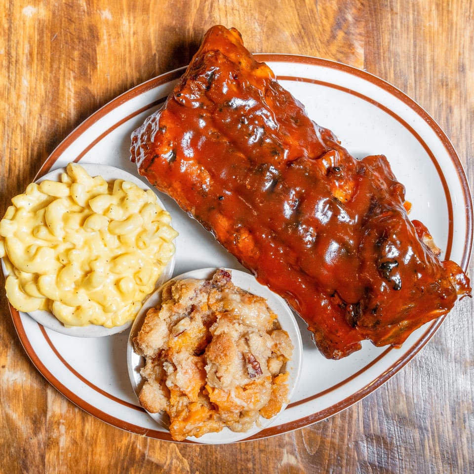 Plate of BBQ ribs with macaroni and cheese and sweet potato casserole on a wooden table.