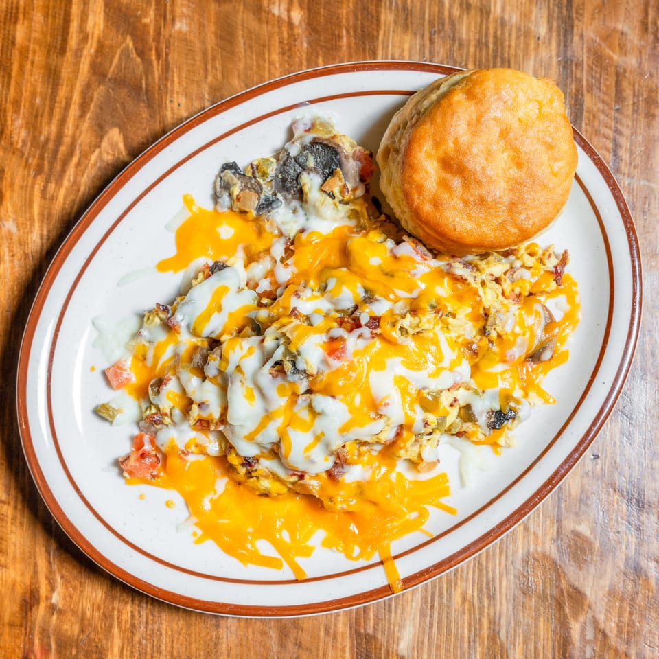 A breakfast plate featuring cheesy scrambled eggs with vegetables and a fluffy biscuit on a wooden surface.