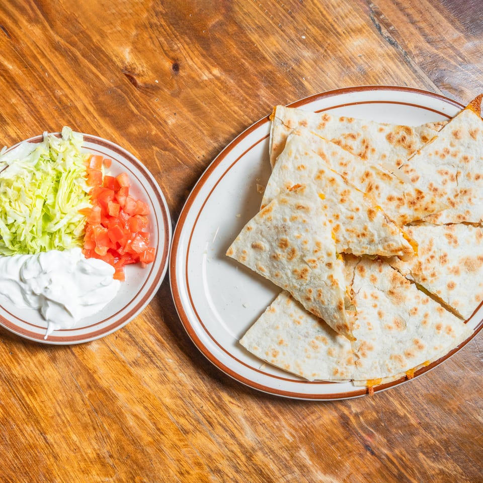 Quesadilla slices and a side of lettuce, tomatoes, and sour cream on a wooden table.